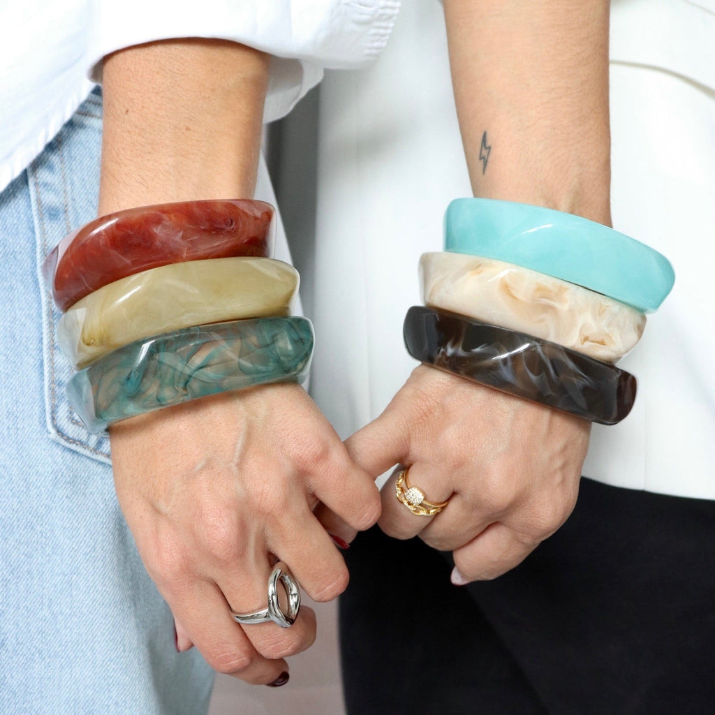 Two people wearing colorful bangles on a neutral background