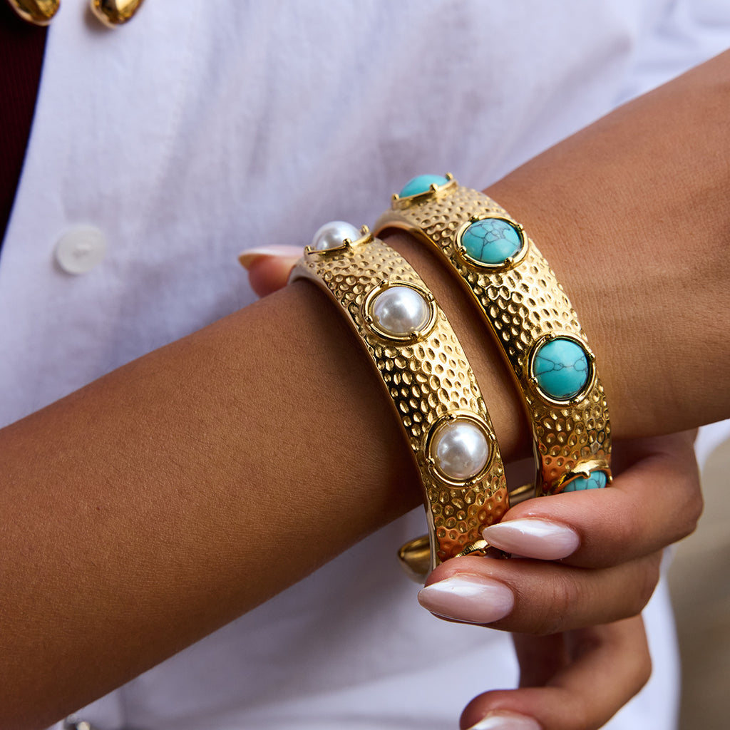 Gold bangles with turquoise and pearl stones on a wrist against a white background