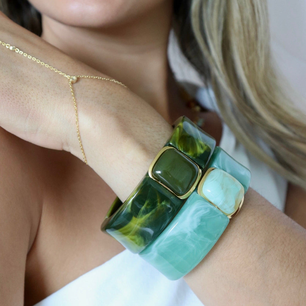 Close-up of a woman's arm wearing a green and gold bracelet with a blurred background.