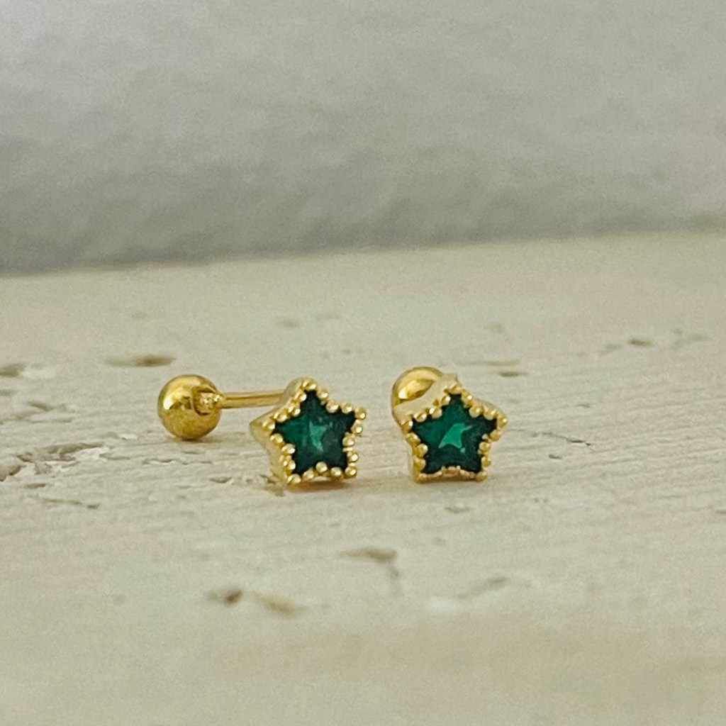 Gold star-shaped earrings with green stones on a light background