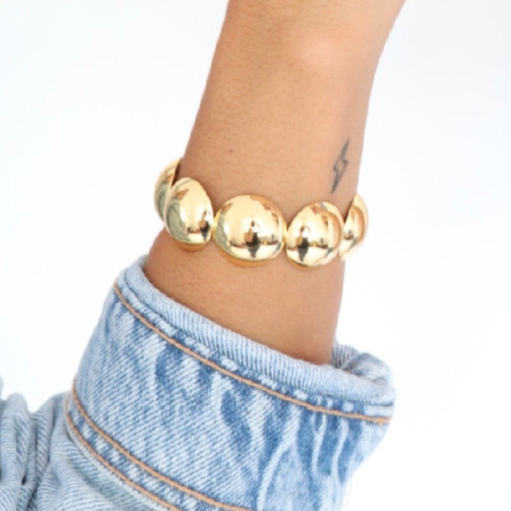 Gold beaded bracelet on a wrist with a light blue denim jacket