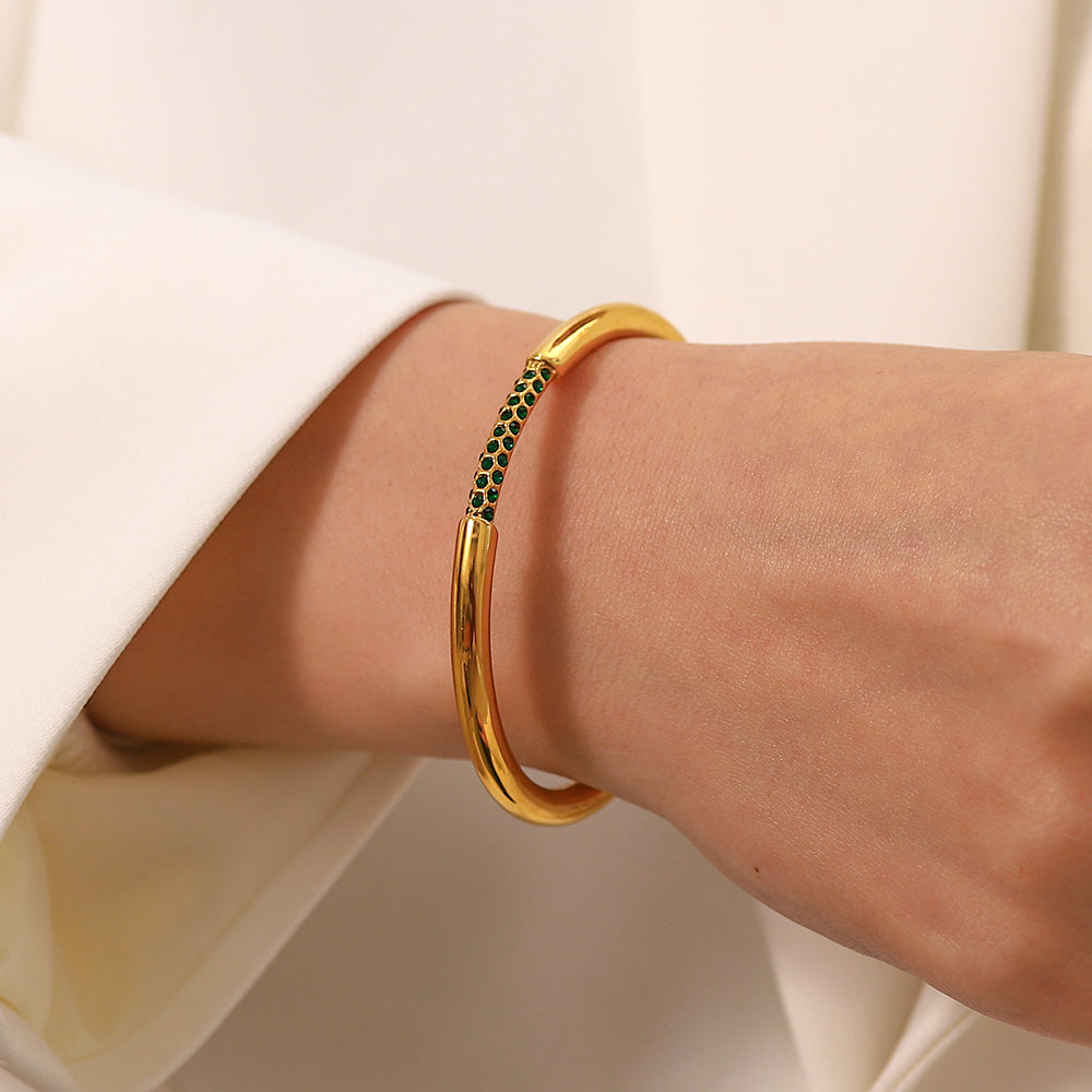 Gold bracelet with green stones on a wrist against a neutral background